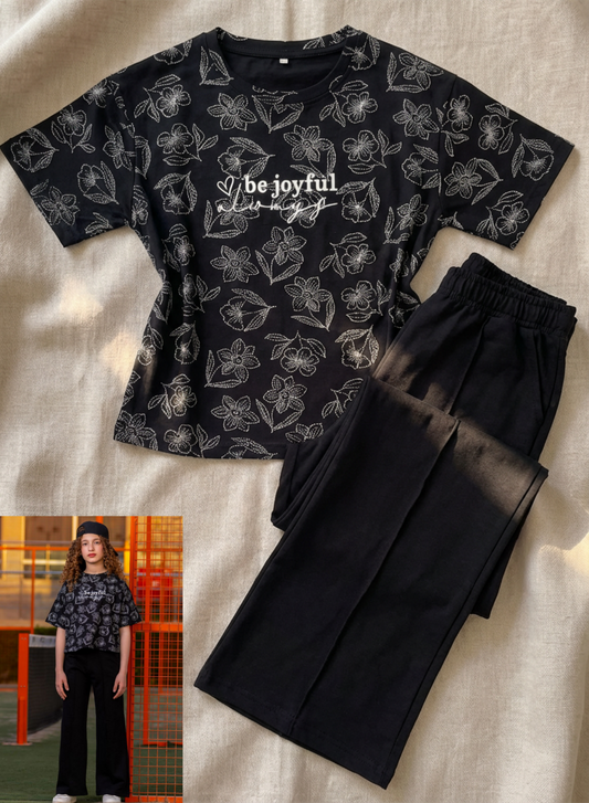 Black t-shirt with floral pattern and text, paired with black pants on a beige background.
